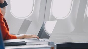 Attractive asian female passenger of airplane sitting in comfortable seat listening music in earphones while working at modern laptop computer with mock up area using wireless connection on board. video
