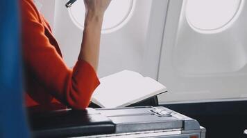 Attractive asian female passenger of airplane sitting in comfortable seat listening music in earphones while working at modern laptop computer with mock up area using wireless connection on board. video