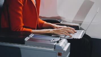 Attractive asian female passenger of airplane sitting in comfortable seat listening music in earphones while working at modern laptop computer with mock up area using wireless connection on board. video