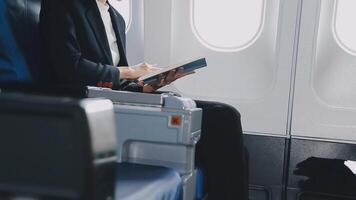 Attractive asian female passenger of airplane sitting in comfortable seat listening music in earphones while working at modern laptop computer with mock up area using wireless connection on board. video