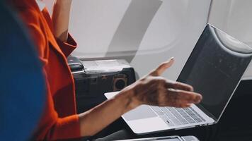 Attractive asian female passenger of airplane sitting in comfortable seat listening music in earphones while working at modern laptop computer with mock up area using wireless connection on board. video