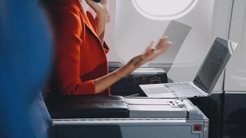 Attractive asian female passenger of airplane sitting in comfortable seat listening music in earphones while working at modern laptop computer with mock up area using wireless connection on board. video