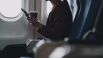 Attractive asian female passenger of airplane sitting in comfortable seat listening music in earphones while working at modern laptop computer with mock up area using wireless connection on board. video