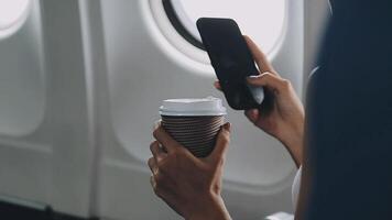Woman hand using smart phone on airplane. Female traveler using smart phone in passenger cabin. Can be add your texts or others on screen. Sun shining trough airplane window. Technology concept. video