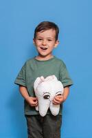 A smiling boy with healthy teeth holds a plush tooth in his hands on a blue isolated background. Oral hygiene. Pediatric dentistry. Prevention of caries. vertical snapshot photo