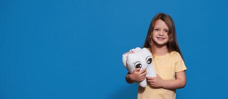 A smiling girl with healthy teeth holds a toy tooth and a toothbrush on a blue isolated background. A place for your text. Oral hygiene. Pediatric dentistry. Prosthetics. Rules for brushing teeth. photo