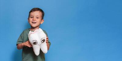 A smiling boy with healthy teeth holds a plush tooth in his hands on a blue isolated background. Oral hygiene. Pediatric dentistry. Prevention of caries. A place for your text. photo
