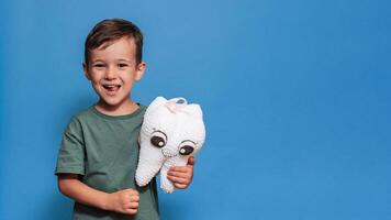 A smiling boy with healthy teeth holds a toothbrush and a plush tooth on a blue background. Pediatric dentistry. A place for your text. Panoramic photo. photo