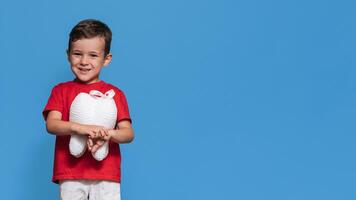 A smiling boy with healthy teeth holds a plush tooth in his hands on a blue isolated background. Oral hygiene. Pediatric dentistry. Prevention of caries. A place for your text. photo