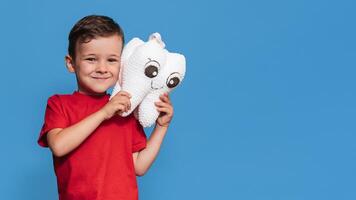 A smiling boy with healthy teeth holds a plush tooth in his hands on a blue isolated background. Oral hygiene. Pediatric dentistry. Prevention of caries. A place for your text. photo