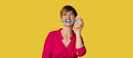 A young Caucasian woman with an amazing smile with a toothbrush in her hands on a yellow isolated background. Plastic jaws. A place for your text. photo