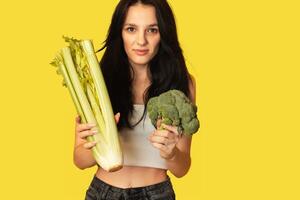 Smiling slender Caucasian girl with green vegetables in her hands, broccoli and celery. Organic vegetables. photo
