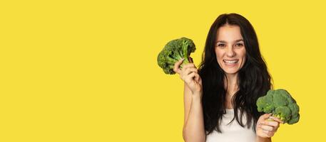 Broccoli in the hand of a slender smiling Caucasian young woman on a yellow background. healthy lifestyle. Panorama, a place for text photo