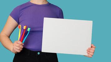 A close-up of a set of colorful toothbrushes and a blank sheet in women's hands to write text on it. Panoramic banner photo