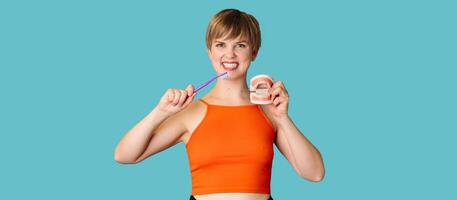 A smiling young woman with a jaw model and a toothbrush on an isolated blue background. Orthodontics. A panoramic image with a copy of the space. photo