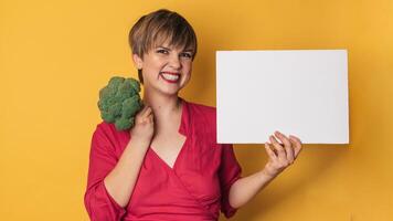 A studio shot of a young smiling woman holding fresh broccoli and a blank letterhead. The concept of healthy eating. A place for your text. Panoramic banner. photo