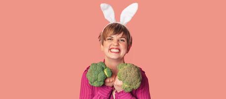 Studio shot of a young Caucasian woman in bunny ears holding fresh broccoli in her hands. healthy eating.A panoramic banner with a copy of the space. photo