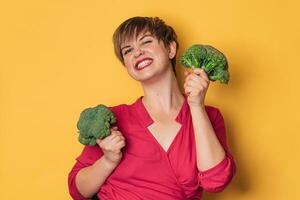 Broccoli in the hand of a slender smiling woman on a yellow background. healthy lifestyle. photo