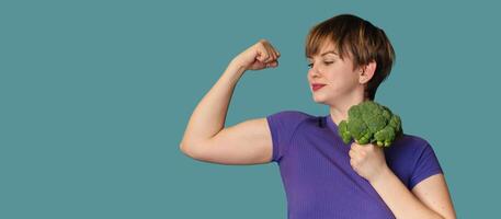 A happy, excited, funny young Caucasian woman doing exercises with broccoli dumbbells, standing against an isolated background, smiling. A panoramic banner with a place for text. photo