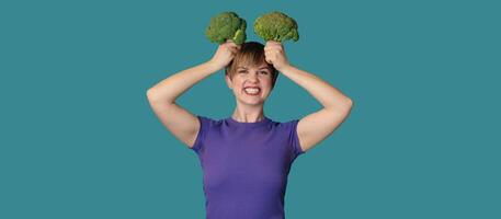 In the studio picture, a young Caucasian woman is holding fresh broccoli in her hands, and on top of her head. The concept of healthy eating. A place for your text. Panoramic banner. photo