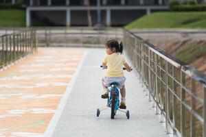 Back side view of asian baby girl child learning to ride bicycle in the park garden. Education concept for kid practiice cycling at park, baby sport concept. photo