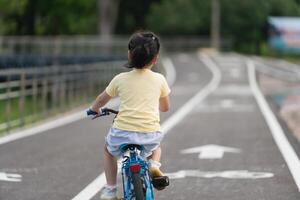 Back side view of asian baby girl child learning to ride bicycle in the park garden. Education concept for kid practiice cycling at park, baby sport concept. photo