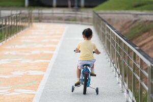 Back side view of asian baby girl child learning to ride bicycle in the park garden. Education concept for kid practiice cycling at park, baby sport concept. photo
