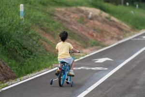 Back side view of asian baby girl child learning to ride bicycle in the park garden. Education concept for kid practiice cycling at park, baby sport concept. photo