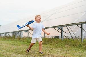 Little happy boy playing with toy airplane near solar panels. photo