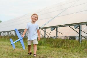 Little happy boy playing with toy airplane near solar panels. photo