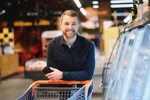 Handsome man buying some healthy food and drink in modern supermarket or grocery store. Lifestyle and consumerism concept. photo