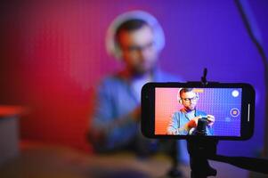 Panoramic view of young adult vlogger creating internet content, holding carton box in hands, unpacking received pack and recording media online on broadcast equipment photo