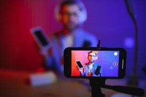 Male technology blogger recording blog or vlog review of new smartphone, showing it on camera at home studio. Blogging, Work from Home concept. Selective focus. Web Banner photo