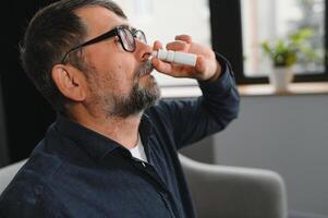 Illness And Sickness. Closeup Of man Feeling Sick Dripping Nasal Drops In Blocked Nose. Portrait male Sprays Cold And Sinus Medicine In Runny Nose. Sinusitis treatment photo