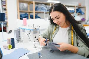 Cheerful young seamstress sits at the table with working things, in atelier photo