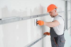man drywall worker using trowel for plasterer putting stucco on plasterboard white wall. photo