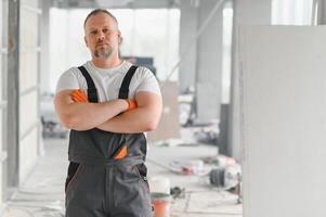 Portrait of a builder in working uniform with protective helmet standing with instruments at the construction site indoors photo