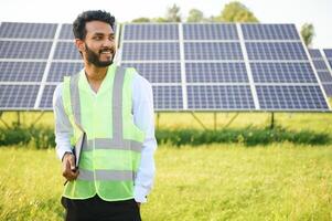 Portrait of Young indian male engineer standing near solar panels, with clear blue sky background, Renewable and clean energy. skill india, copy space. photo