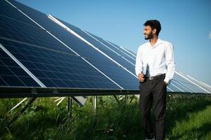 Portrait of Young indian male engineer standing near solar panels, with clear blue sky background, Renewable and clean energy. skill india, copy space. photo