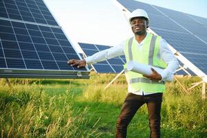 Close up portrait of young african american engineer worker in hardhat holding solar plan. Green electricity future concept. photo