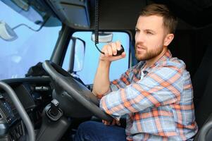 Man trucker driving in a cabin of his truck and talking on radio transmitter. photo