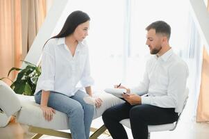 Psychologist taking notes during therapy session with sad young woman in his office. Copy space photo