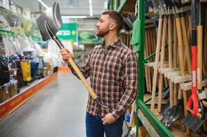 Portrait of a happy young man and customer buying a shovel while shopping at the hardware store photo