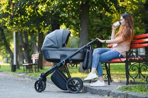 Happy young mother with baby in buggy sitting on bench in autumn park photo