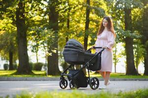 family, child and parenthood concept - happy mother walking with baby stroller in park. photo