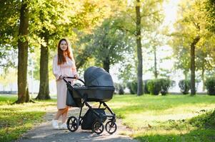 Happy young mother with baby in buggy walking in autumn park photo