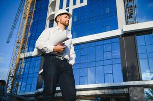 Successful engineer or architect, crane and building construction at backgrpound. Joyous businessman wearing helmet photo