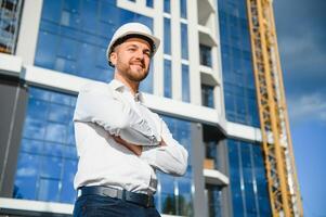 Portrait of a smiling male contractor engineer with hard hat reading blueprint at construction site. photo