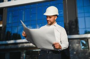 Successful engineer or architect, crane and building construction at backgrpound. Joyous businessman wearing helmet photo