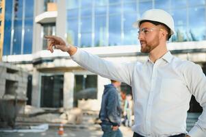 Successful engineer or architect, crane and building construction at backgrpound. Joyous businessman wearing helmet photo
